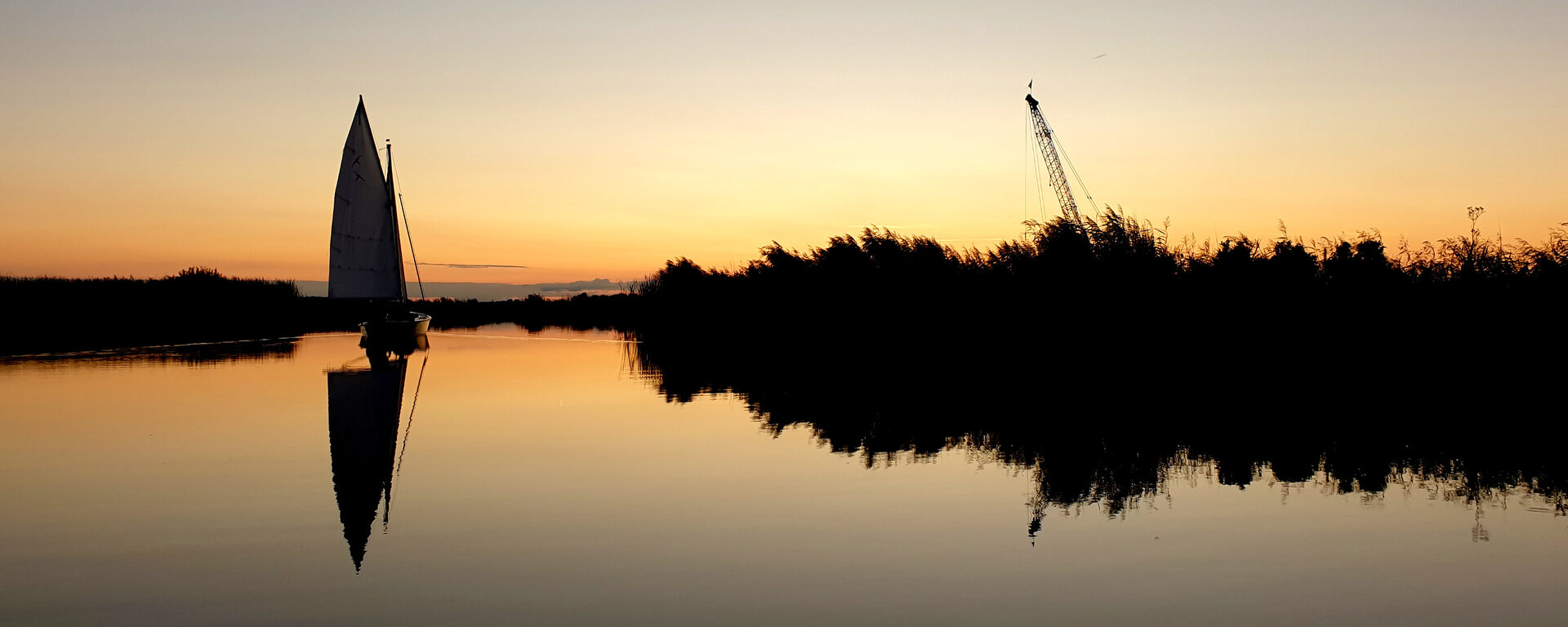 Ein Segelboot fährt auf einem Kanal in Friesland auf einen spektakulären Sonnenuntergang zu.